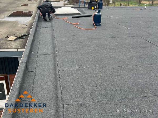 Dakdekker repareert bitumen dakbedekking op groot plat dak in Susteren